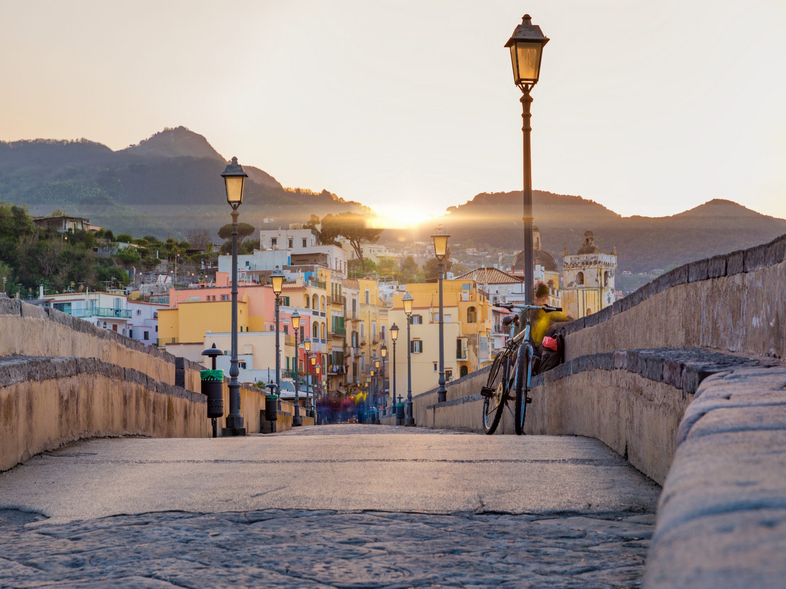 Sunset view from side of Aragonese Castle on Ischia street with colourful houses, Ischia Island, Italy. People blurred due to very long exposure time.